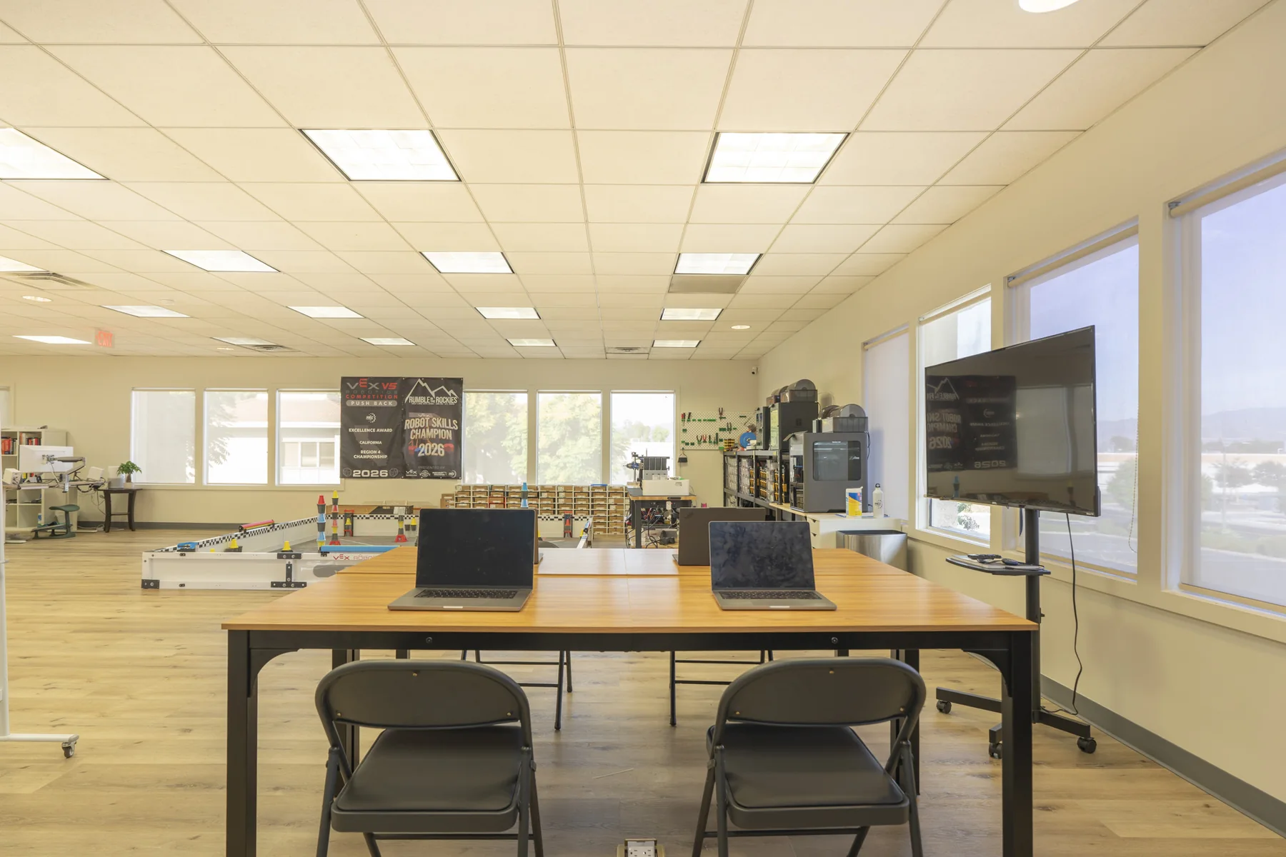 Classroom tables with laptops and a wall screen.