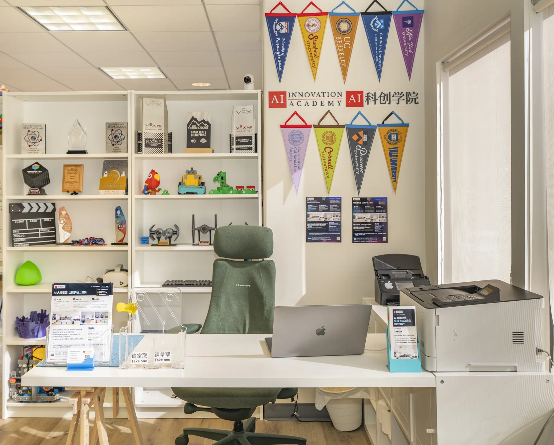 The academy wall with pennants, shelves of student builds and a desk.